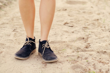 Female legs in blue boots on the sandy dusty road in summer day