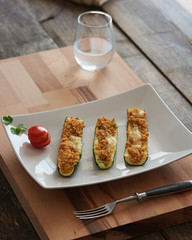 stuffed courgette on a white sqare plate in a rustic enviroment.