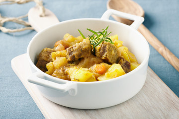 Sicilian stew in a white pot on a blue table, pastel color