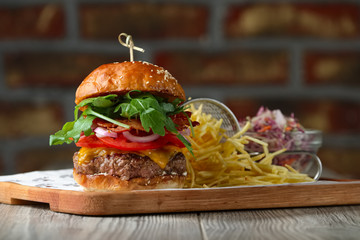Burger on the wooden table with cheese, bacon, tomatos, green an