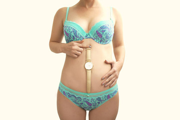Pregnant woman in underwear holding a clock on his stomach. The creative concept on the theme of...