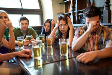 friends with beer watching football at bar or pub