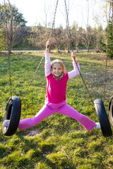 Girl in pink swinging on a tire swing at the park.