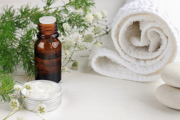 Fototapeta na wymiar Herbal skincare spa setting. Essential oil, skincare cream, white bathroom towel and stones, fresh herb decor. Place for cosmetic product.