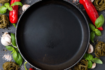 Frying pan on the stone counter surrounded by fresh vegetables, hot spices and pasta