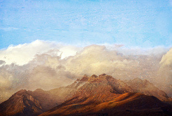 Sun kissed rugged mountain range in the clouds. Grunge wood textured image.