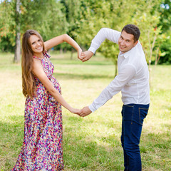 Fototapeta na wymiar Beautiful pregnant couple happy together expecting a child. Man and woman walking in the park showing heart with hands. Share the love and family, love concept.