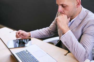 Business man working at table on his laptop and electronic tablet with graphics on the screen deep...
