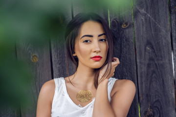 Girl brunette in a park in the summer resting white blouse on the background of  wooden fence, fashion lifestyle, gentle look. Sensual make-up, tanned skin and bright red lipstick.