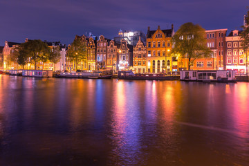 Fototapeta na wymiar Amsterdam canal Amstel with typical dutch houses and houseboats with multi-colored reflections at night, Holland, Netherlands.