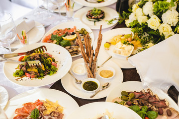 Fototapeta na wymiar Table served with different food and flatware for dinner. Close up of many snacks, appetizers and salads on table waiting for guests. Wedding reception or family event diner in expensive restaurant.