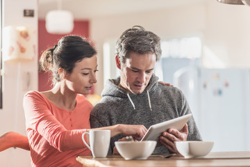 Nice couple using a tablet while having breakfast in the kitchen