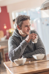 man with gray hair takes breakfast in his cosy kitchen 