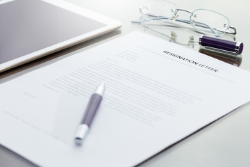 Business man signing his resignation letter on his desk before sending to his boss to quit a job. Resignation letter information with digital tablet and eye glasses