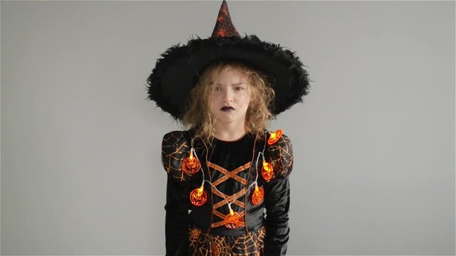 Trick or Treat. Halloween Party. Girl shows the evil sorceress. Child is wearing a black-and-orange dress and hat. From under his hat sticking disheveled hair
