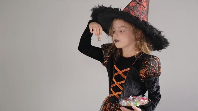 Girl wearing a black-orange dress and a big hat. Girl holds sweets in hands. Trick or Treat, Halloween Party