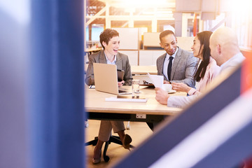 Business meeting between four executives in modern office space with both male and female employees...