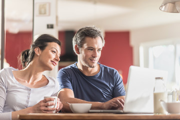 A couple using a laptop while having breakfast in the kitchen