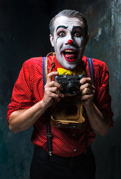 The scary clown and a camera on dack background. Halloween concept