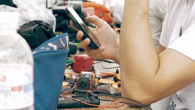 Man using smartphone while assembling FPV drone process, preparing quadcopter for flight. Repair drone before training process.