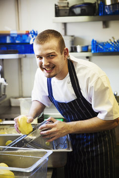 A village public house kitchen. A chef in apron working, using a mandolin cutter on potatoes. 