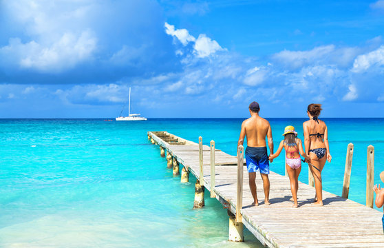 Back view of a happy family on tropical beach. Family standing on a wooden pier.