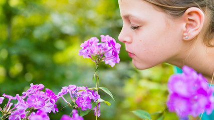 Young beautiful girl smells purple flowers in the garden - shallow depth of field