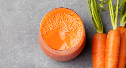 Carrot juice in glass and fresh carrots Healthy food on a grey stone background Top view