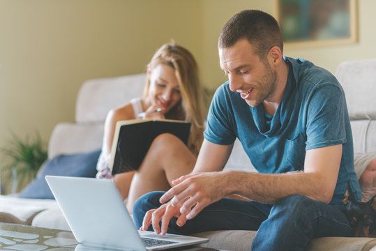 Young Smiling Couple Working At Home  With Laptop And Smartphone.