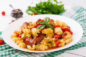 Pasta with tomato sauce with sausage, tomatoes, green basil decorated in white plate on a wooden background.