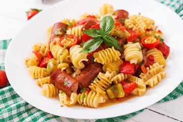 Pasta with tomato sauce with sausage, tomatoes, green basil decorated in white plate on a wooden background.