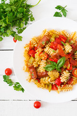 Pasta with tomato sauce with sausage, tomatoes, green basil decorated in white plate on a wooden background. Top view