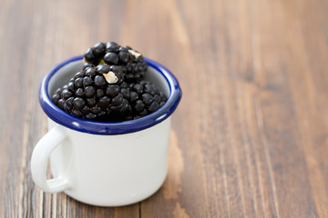Fototapeta na wymiar blackberries in white cup on brown .wooden background