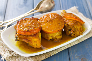 roasted chicken with oranges on white dish on blue wooden background