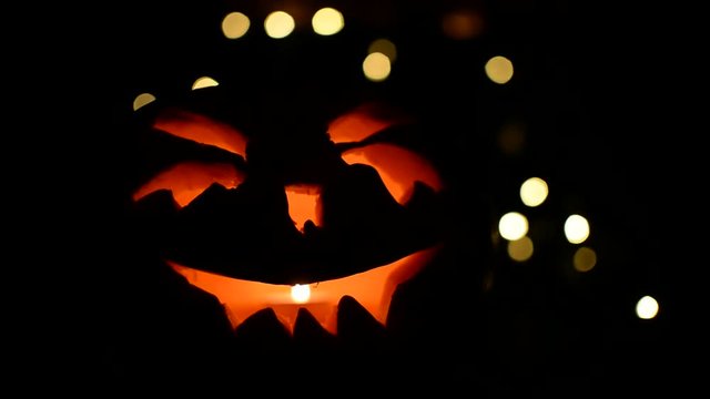 carved face of pumpkin glowing on Halloween on bokeh light background