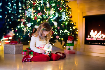 Little girl holding snow globe under Christmas tree