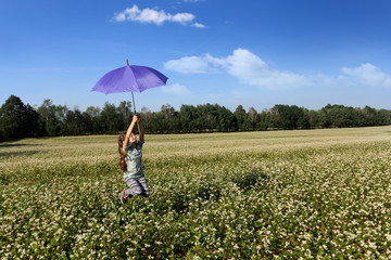 Piękna dziewczynka skacze na łące z parasolem.