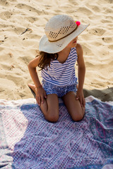 fille avec un chapeau assise dans le sable à la plage