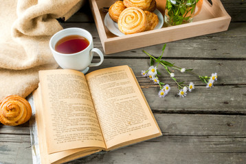 Cozy breakfast in spring or early autumn tea, freshly baked scones and bouquet of field's daisy and fascinating book.