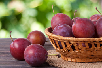 plum in a wicker basket on the wooden table with sackcloth and blurred green background
