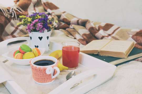 Breakfast in bed with hot coffee and macaroons. Healthy breakfast kept on bed with books and flowers Close up of a cup of coffee with cookies, fresh juice and grapefruit on wooden tray in bed. Toned