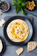 Hummus, chickpea dip, with spices and pita, flat bread in a black plate. Top view