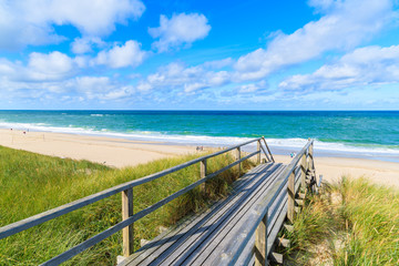 Fototapeta na wymiar Wooden footbridge from sand dune to beautiful beach near Westerland village, Sylt island, Germany