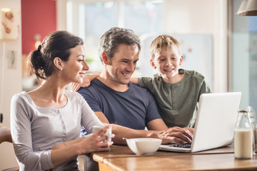 Obraz premium A family using a laptop while having breakfast in the kitchen