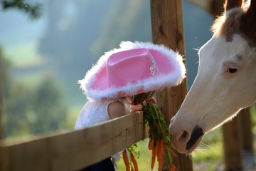 Freunde fürs Leben, kleines Mädchen mit pinkem Cowboyhut füttert geschecktes Pferd