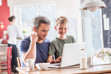 A family using a laptop while having breakfast in the kitchen