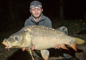 Obraz premium Happy angler with carp fishing trophy. Night fishing.