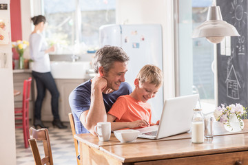  Cheerful father and son using a laptop while having breakfast