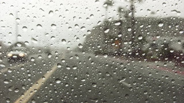 A shot of rain drops collecting on windshield of vehicle driving down a highway. HD 1080p.