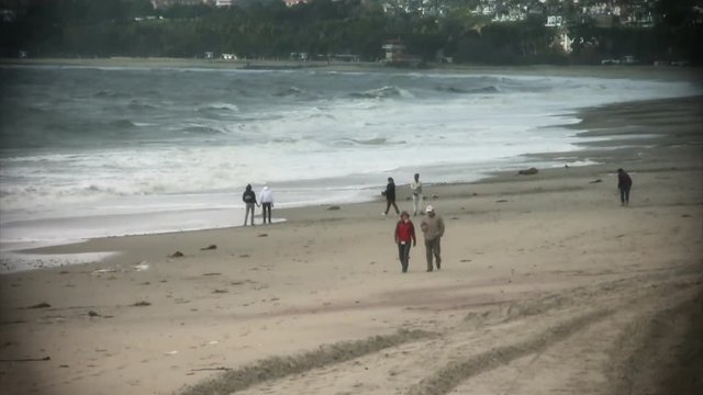 A family plays on beach while an elder couple takes a stroll along the coast. HD 1080.